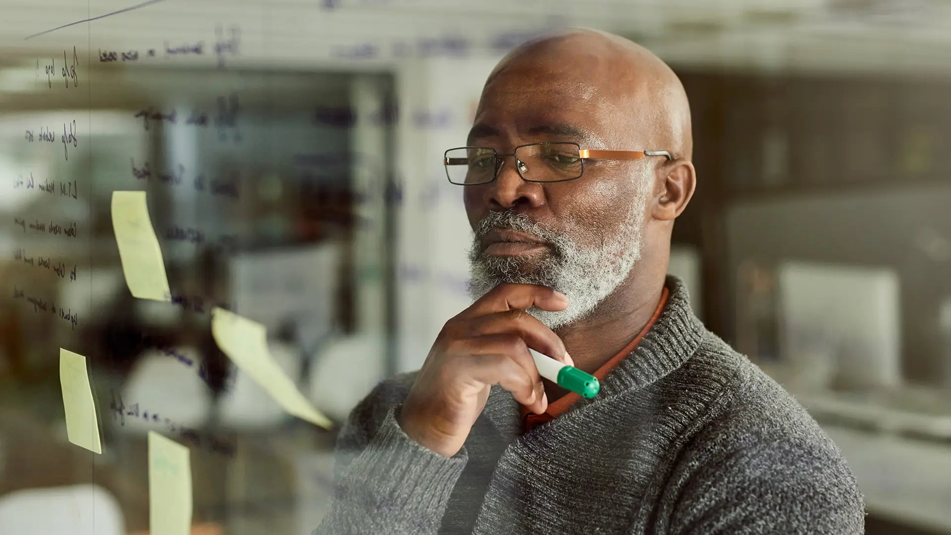 Executive man thinking through ideas on a glass wall with sticky notes